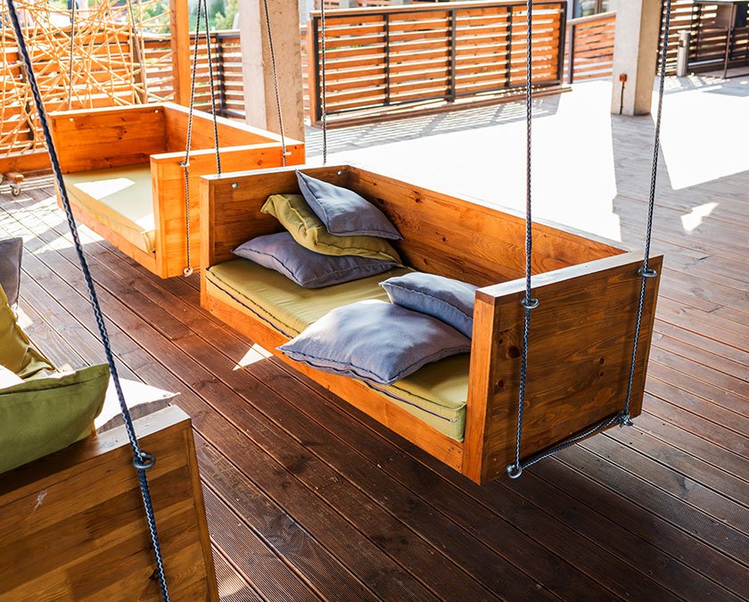 Hardwood deck, with wooden swing couch, and gray pillows.