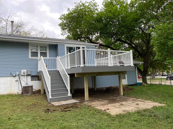 An elevated deck on a light blue house with white railing