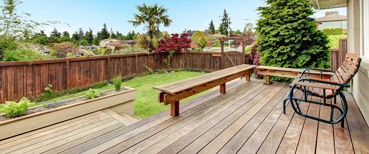 Two chairs on a deck with a patch of grass and a privacy fence