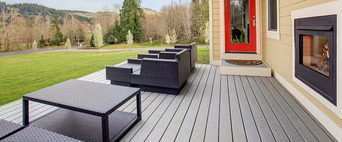 A dark gray composite decking with chairs and table and a red door
