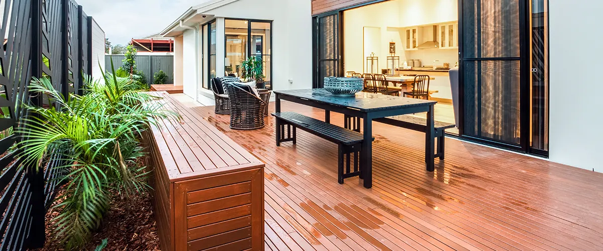 A deck with a wooden bench and black table in front of glass door