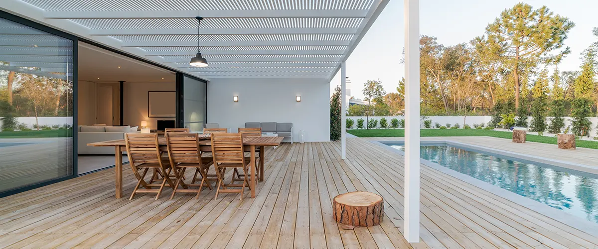 Wooden chairs and table on a wooden deck with a pool and a white cover