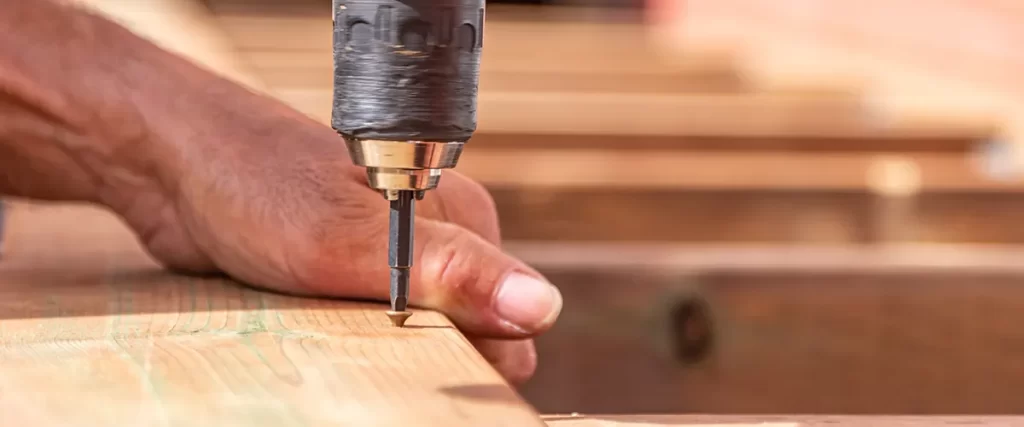 A deck builder using a screw driver on a piece of wood