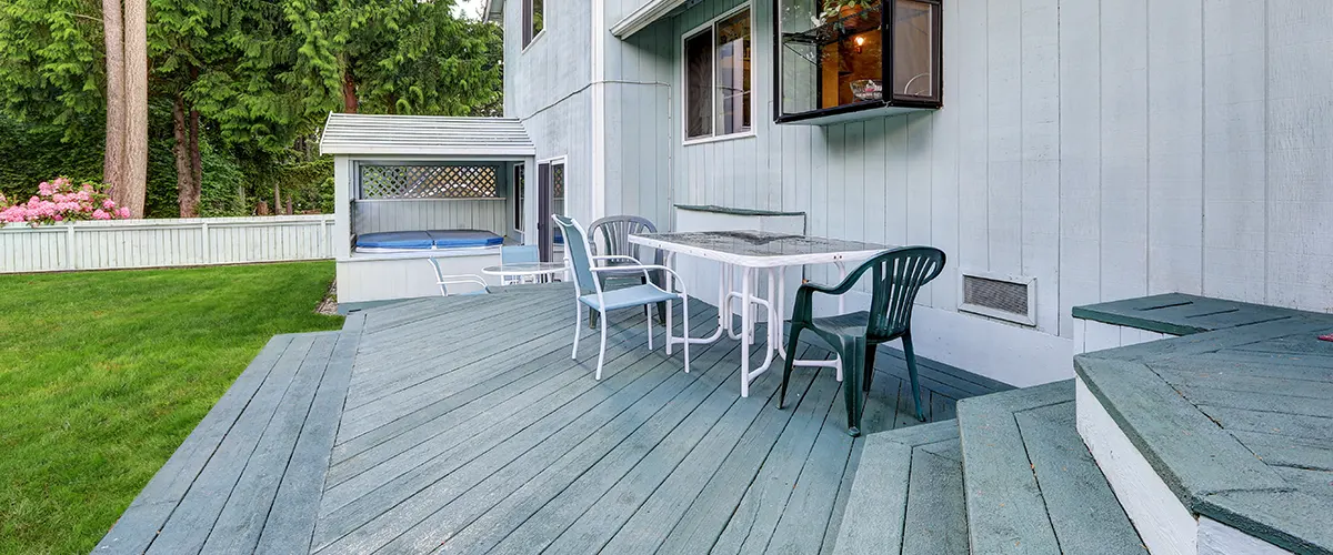 A gray deck at the side of a home with a couple of stairs