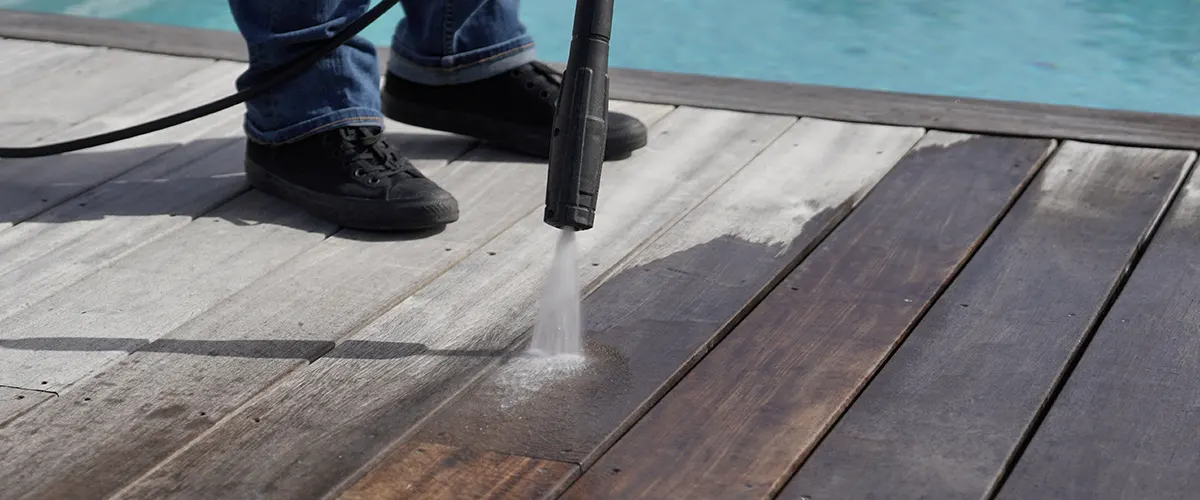 A man pressure washing a wooden deck