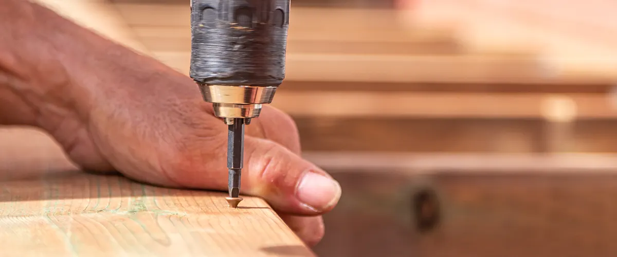 A screwdriver drilling pilot holes on a wood board