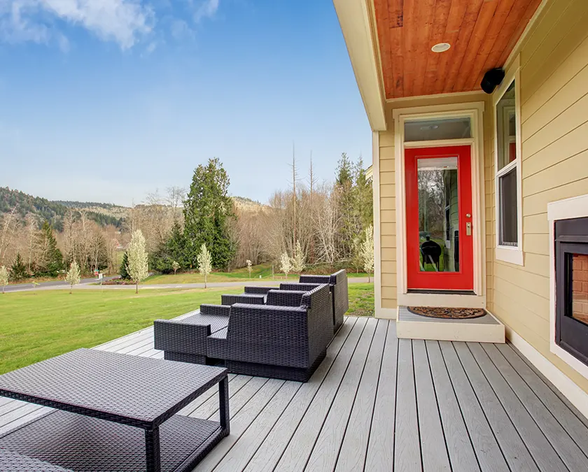 A dark colored composite deck with black chairs and tables and a red door