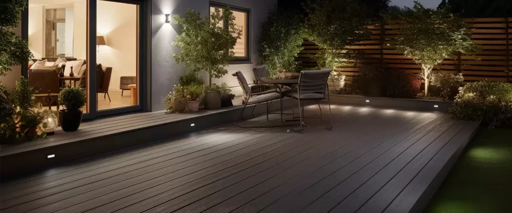 Installing Deck Lighting: Easy & Safe Low-Voltage System Guide Spacious composite deck in the evening featuring recessed low-voltage step lighting and warm landscape uplights illuminating the garden trees and sitting area.