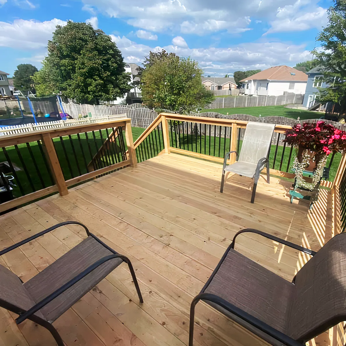 Two black chairs and some flowers on a wood deck with metal and wood railing