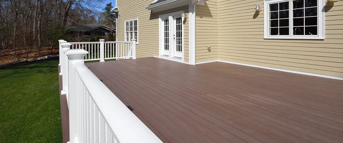 A deck stained in an opaque color with white railings and beige home siding