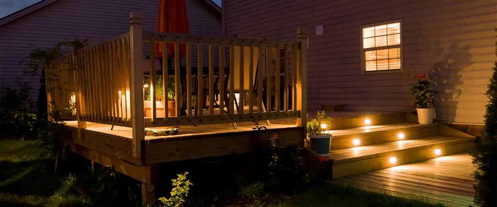 A deck at night with lighting on stairs and on railing