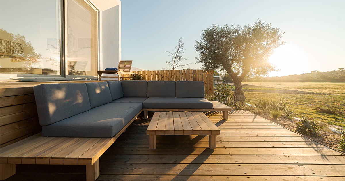 A wooden deck with a wood couch and the sunset behind a tree
