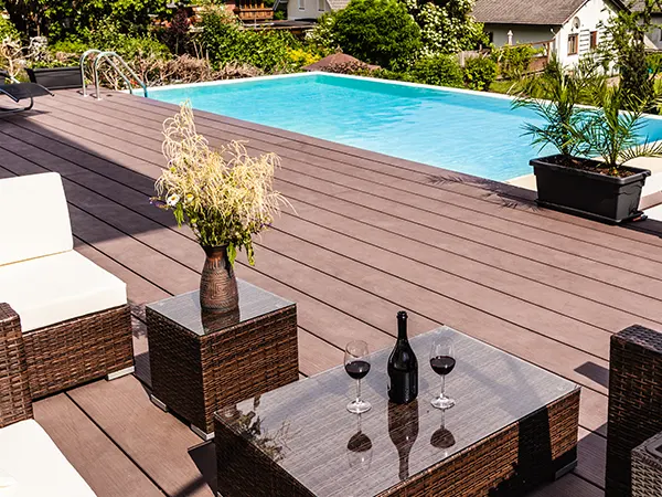 A composite decking near a pool with chairs and a table with a wine bottle