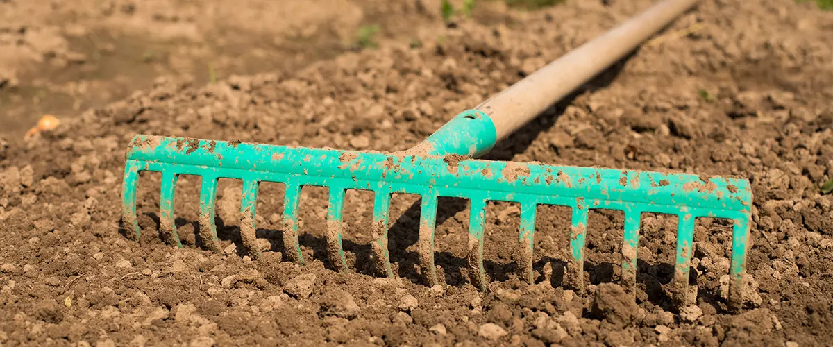 A man using a rake to clean the ground for a deck frame