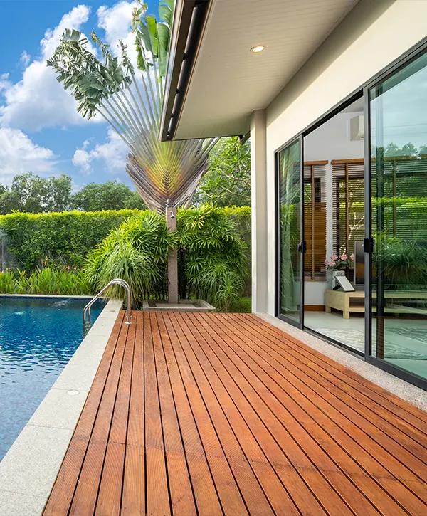 A beige composite pool deck near a home with large windows