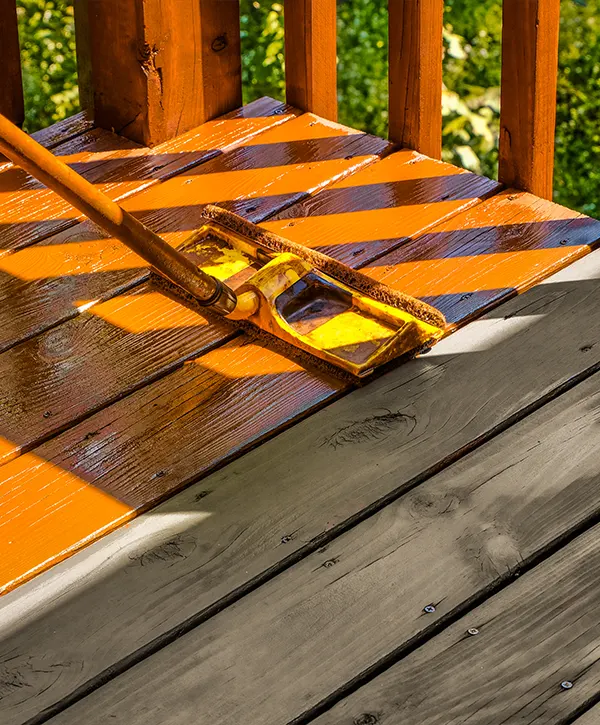 A contractor using a pole to deck stain a deck