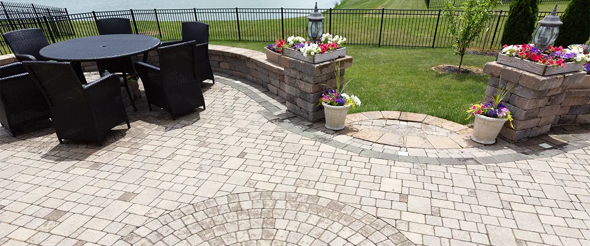 A paver patio with flowers and plastic black chairs and a table