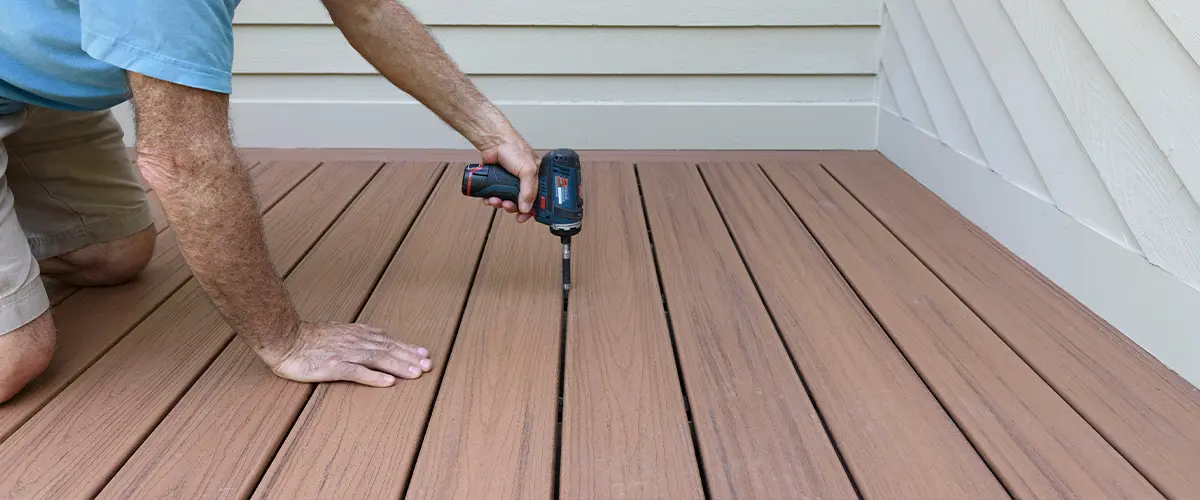 A deck builder screwing down composite decking boards