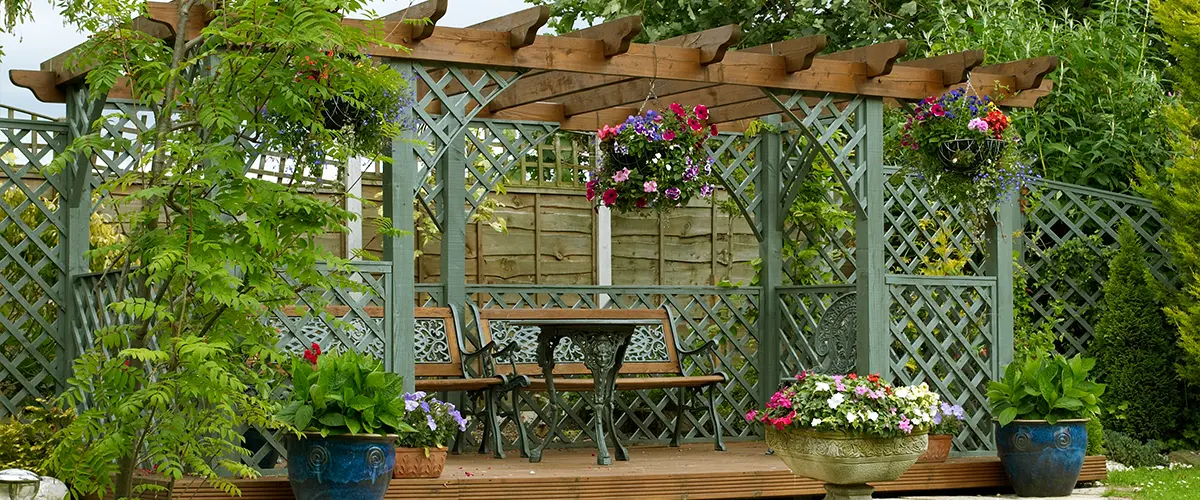 A wooden deck with a green pergola with plants