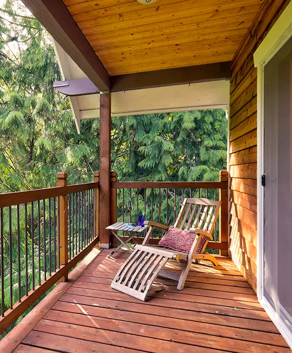 An elevated wood deck with a long chair and a table