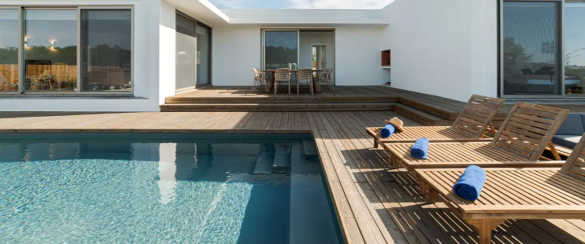 A wood deck with long chairs and a pool