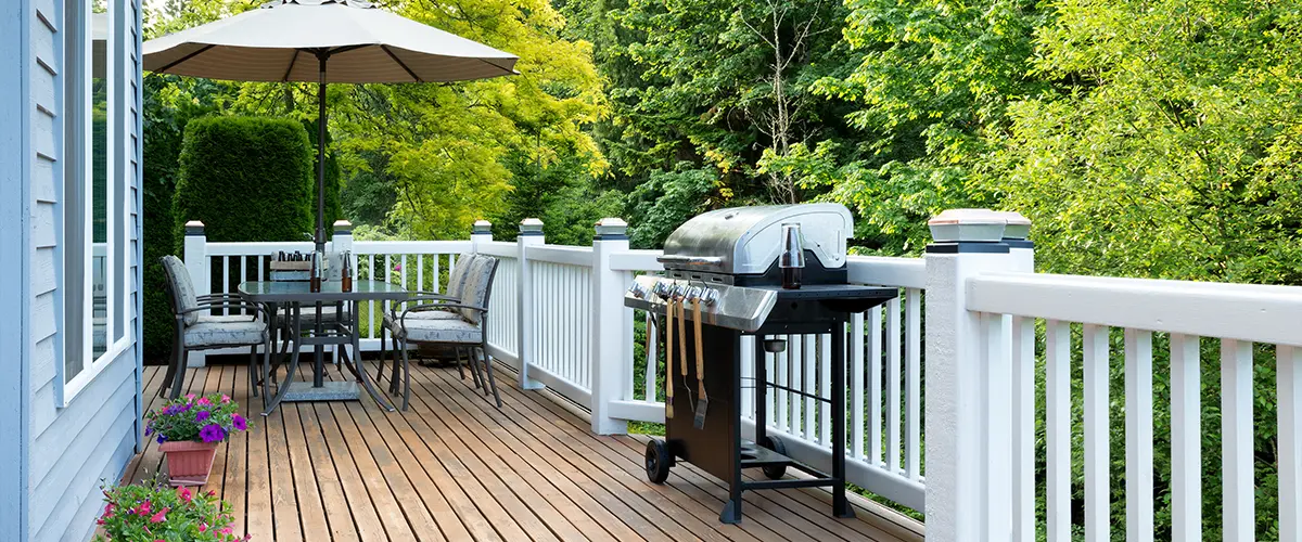 A wood deck with a barbecue and a table with chairs