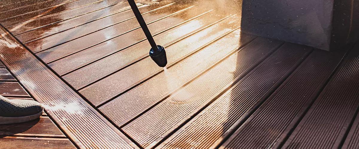 man cleaning terrace with a power washer - high water pressure cleaner on wooden terrace surface