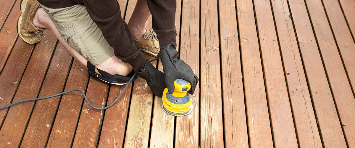 worker in the process of sanding a wooden deck.