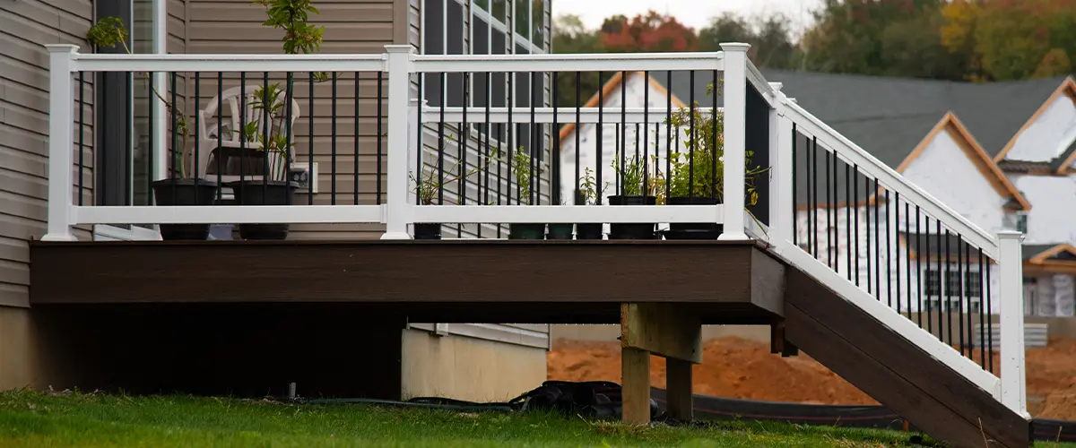 New deck installation with white railing on a brown house overlooking a lush green lawn