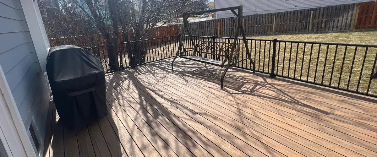 Sunny wooden deck installation with railing and outdoor grill in backyard.