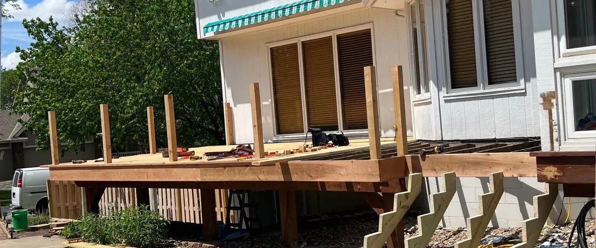 Workers installing wooden planks during a deck installation in a sunny backyard.