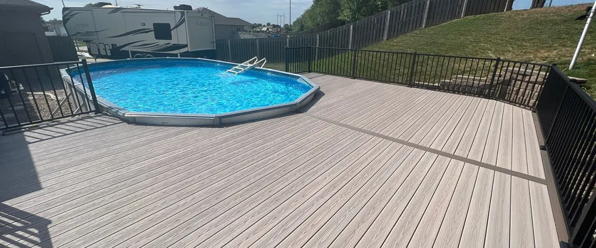 Above-ground pool with wooden deck and fence under clear blue sky