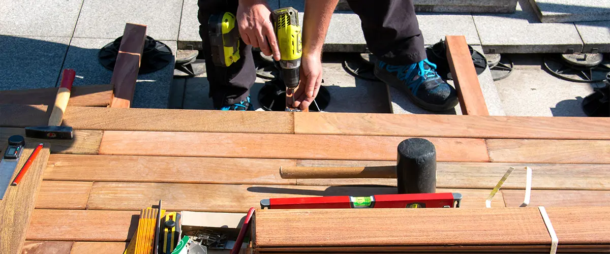 Carpenter using drill on wooden planks at construction site, optimizing deck building. Deck Building Codes In Fremont, NE