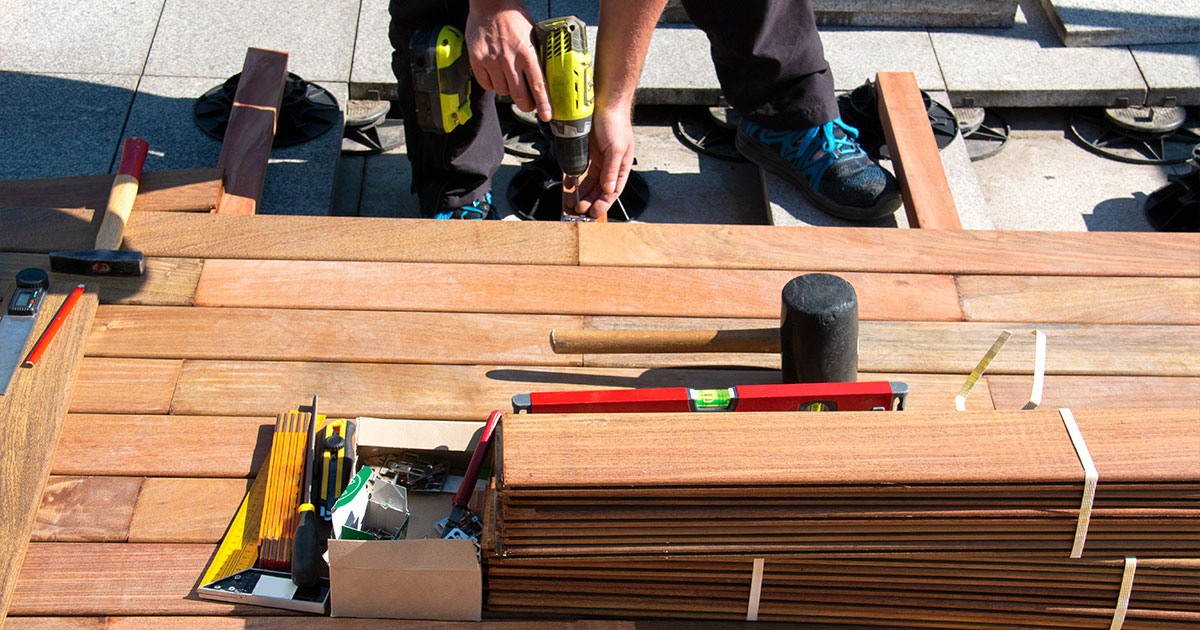 Carpenter using drill on wooden planks at construction site, optimizing deck building. Deck Building Codes In Fremont, NE