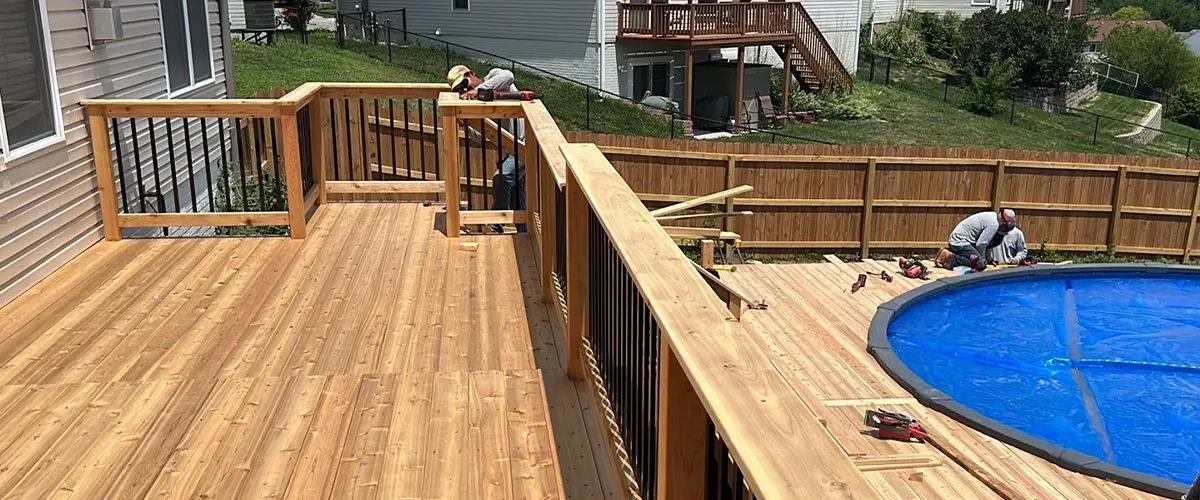 New wooden deck construction with workers and blue pool in suburban backyard. Pool Deck Installation In Omaha, NE