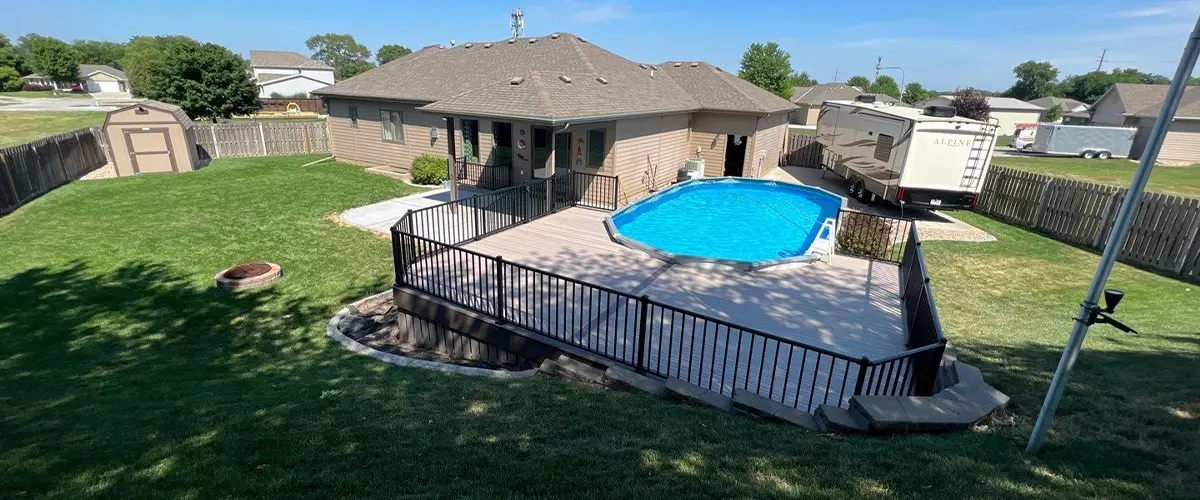 Suburban backyard with decked above-ground pool, lawn, and clear blue sky. Pool Deck Installation In Omaha, NE