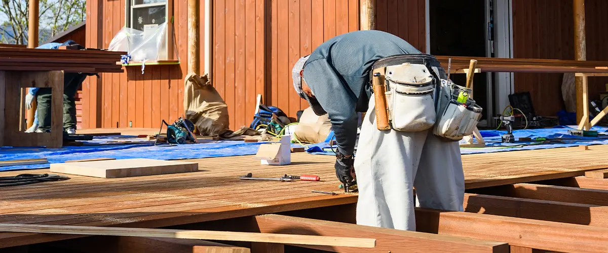 Construction worker building a wooden deck on a house exterior, using tools and equipment for outdoor home improvement.