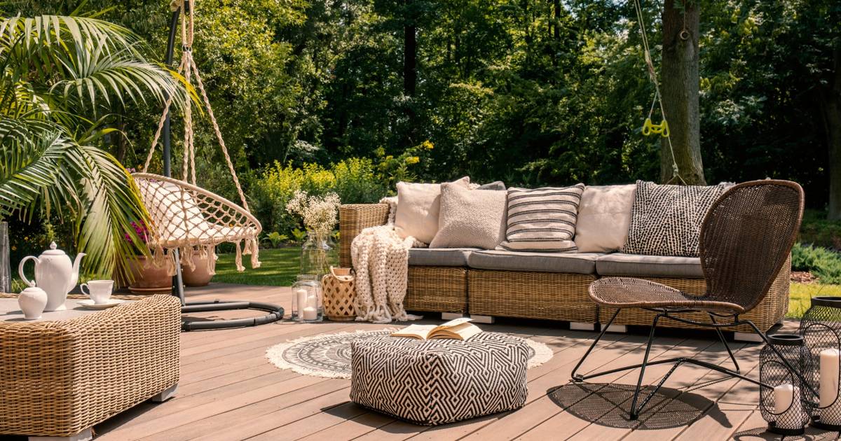 A beautifully designed outdoor deck with rattan furniture, decorative pillows, a hanging chair, and a lush green garden in the background