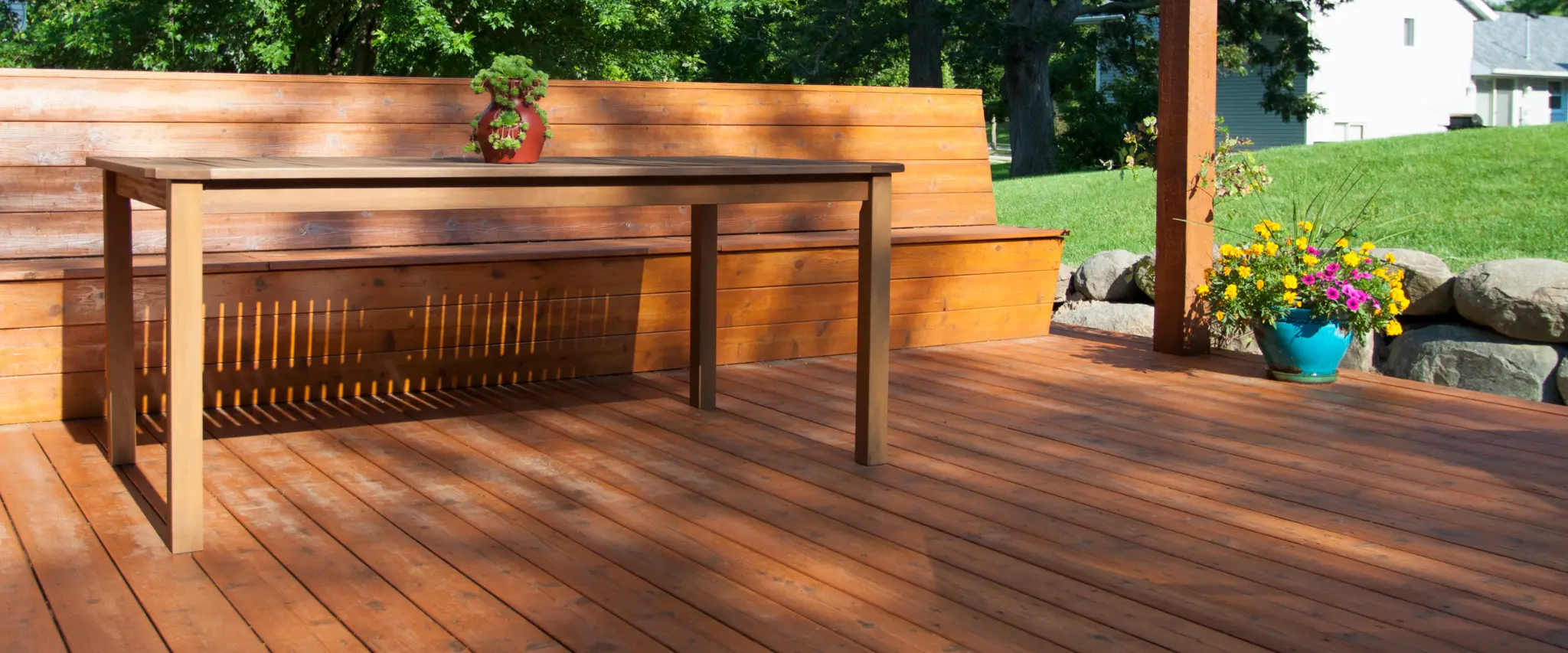 Deck with wooden table, bench, and colorful potted plants for a cozy outdoor space