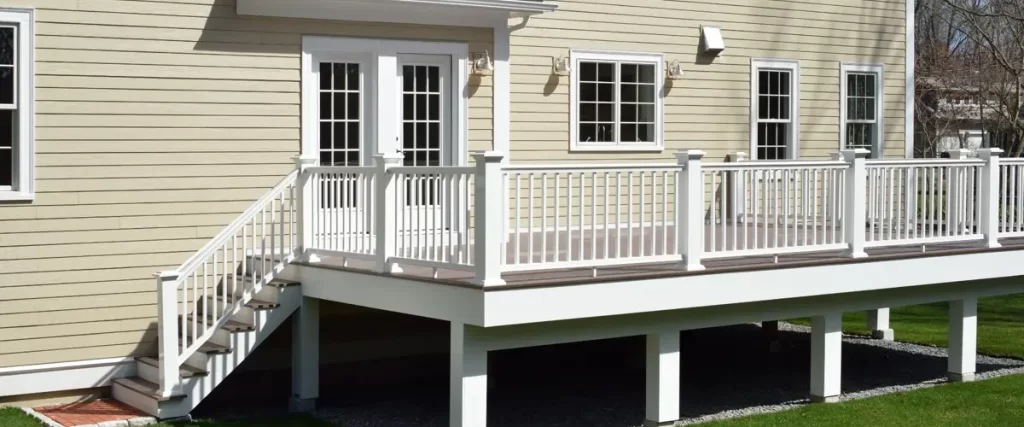 A well-maintained elevated deck attached to a beige house with white railings and stairs leading down to a green lawn