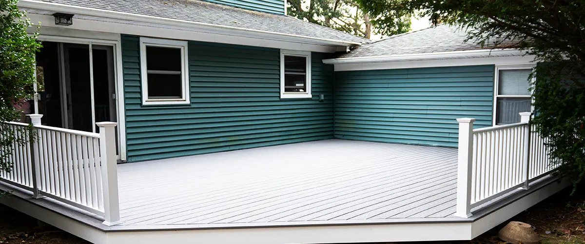 Address Trex deck problems with Omaha's expert deck builders. This image features a clean, modern deck with white railings and a charming teal home exterior.