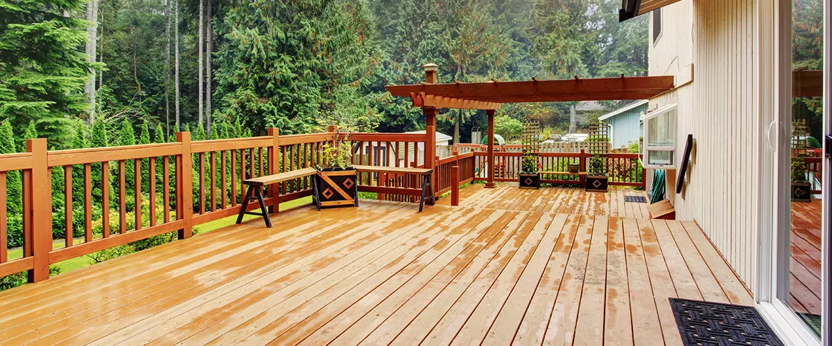 Learn how to apply Thompson’s Water Seal to protect your deck. Pictured: a freshly treated wooden deck with a pergola and lush green surroundings.