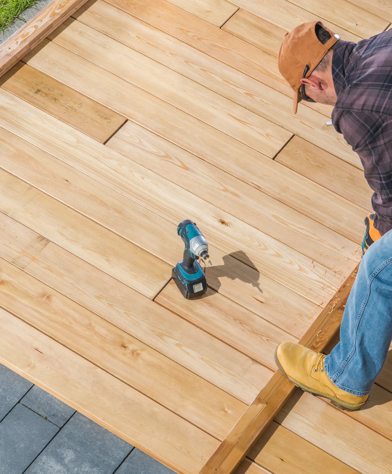 Skilled worker using a drill to install wooden deck boards on a home deck