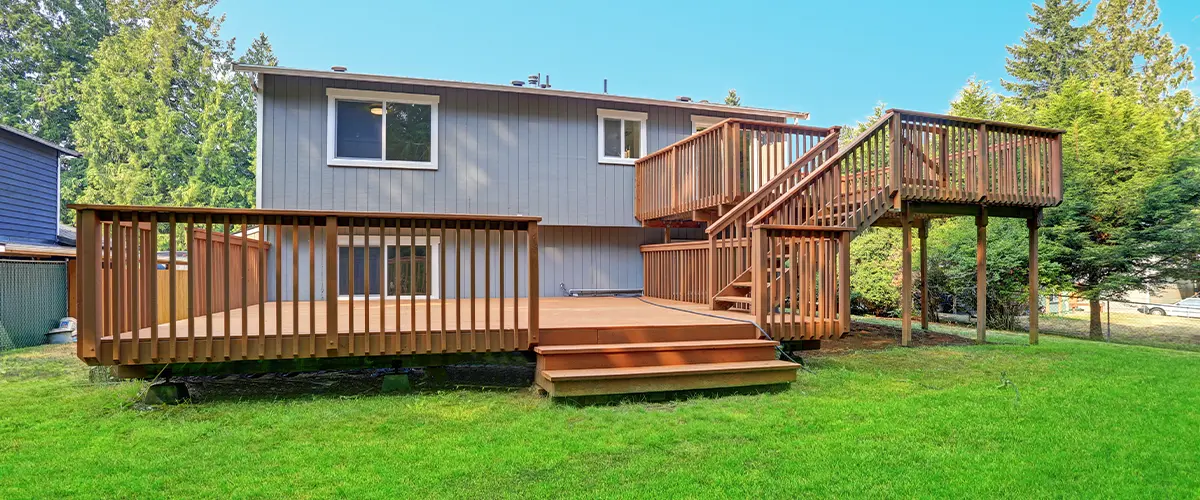 Large multi-tiered wooden deck with railings and stairs, surrounded by lush green trees, designed for outdoor relaxation and entertaining.