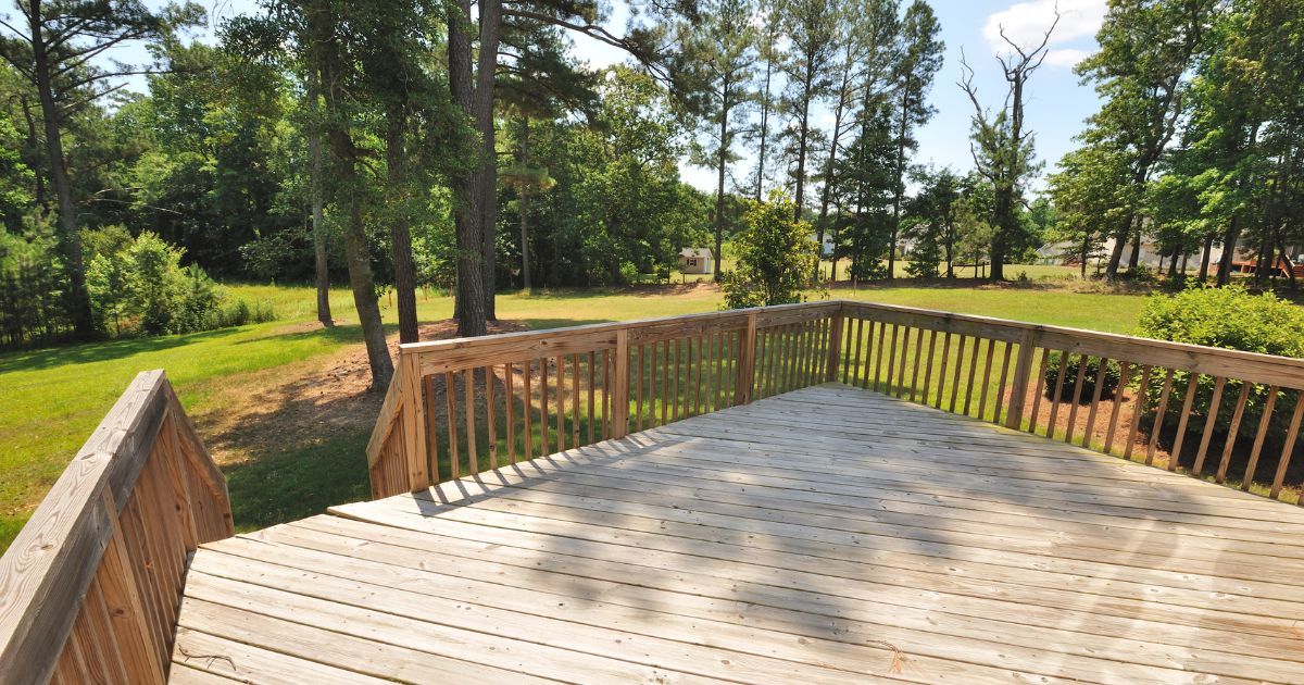 Wooden deck with railings, surrounded by tall trees in a backyard