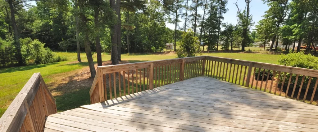 Spacious wooden deck with railings, surrounded by a green yard