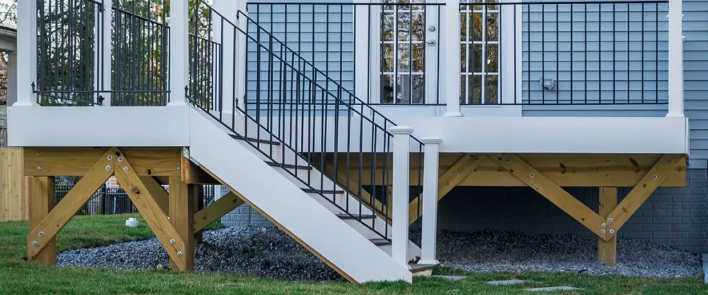 Elevated backyard deck with black metal and white post railings, attached to a blue house with French doors.