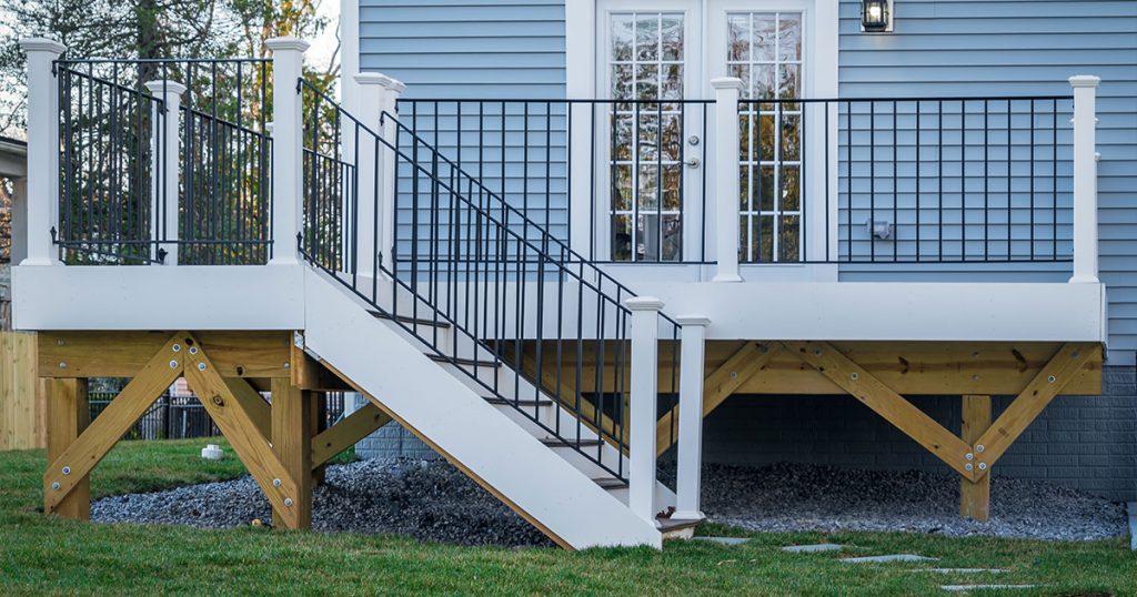 How to Choose the Right Footing for Elevated Decks Elevated backyard deck with black metal and white post railings, attached to a blue house with French doors.