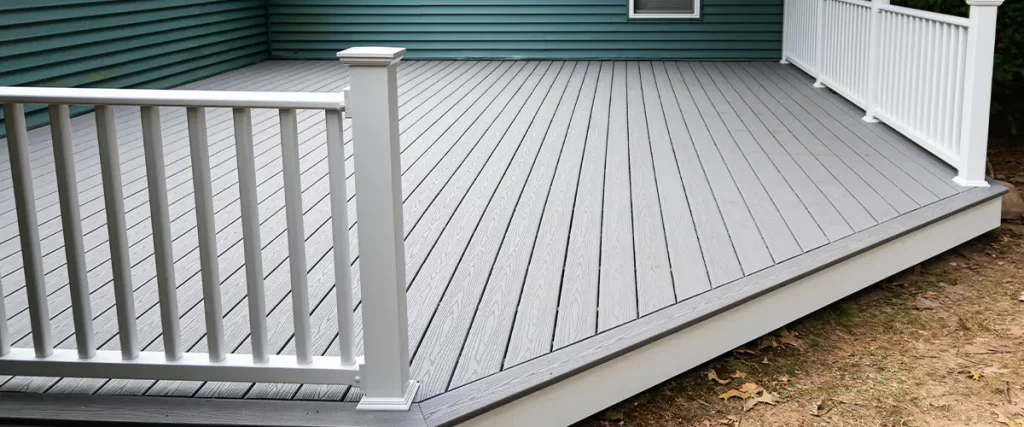 Modern gray composite deck with white railing attached to a green house. Durable, low-maintenance outdoor living space upgrade.