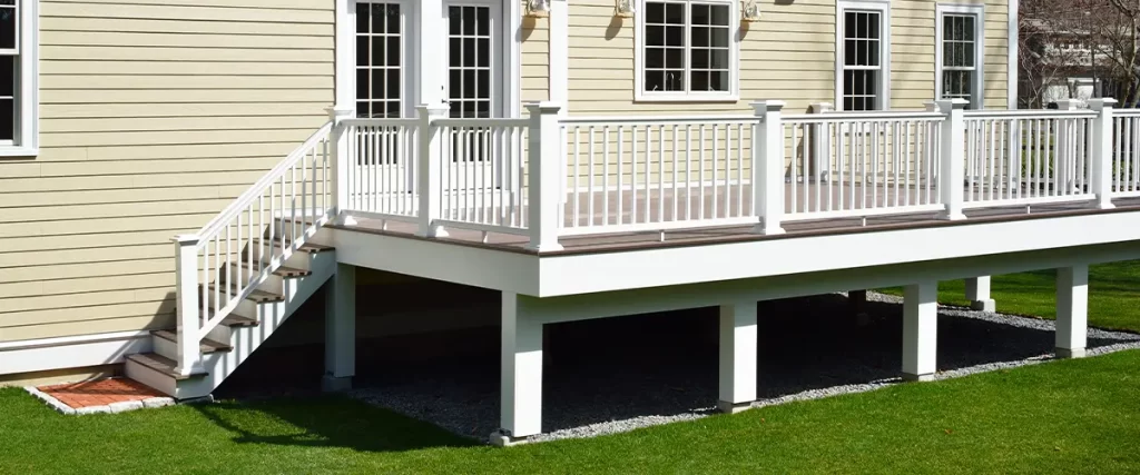 Raised composite deck with white railings attached to beige house, perfect for outdoor living space.